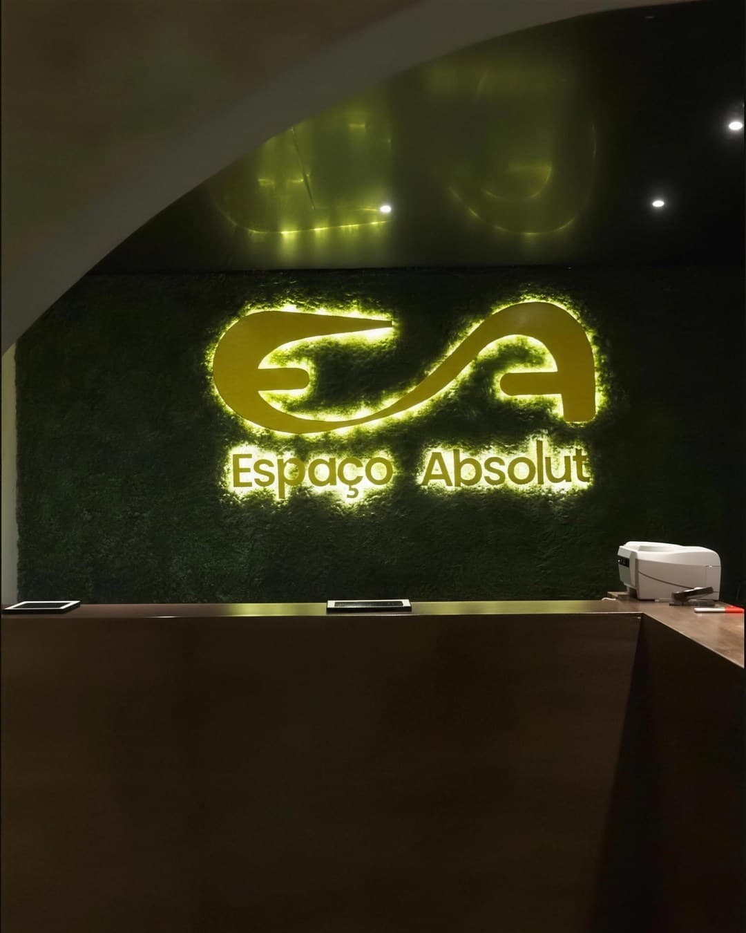 Recepção do Espaço Absolut, com o logo iluminado na parede de musgo